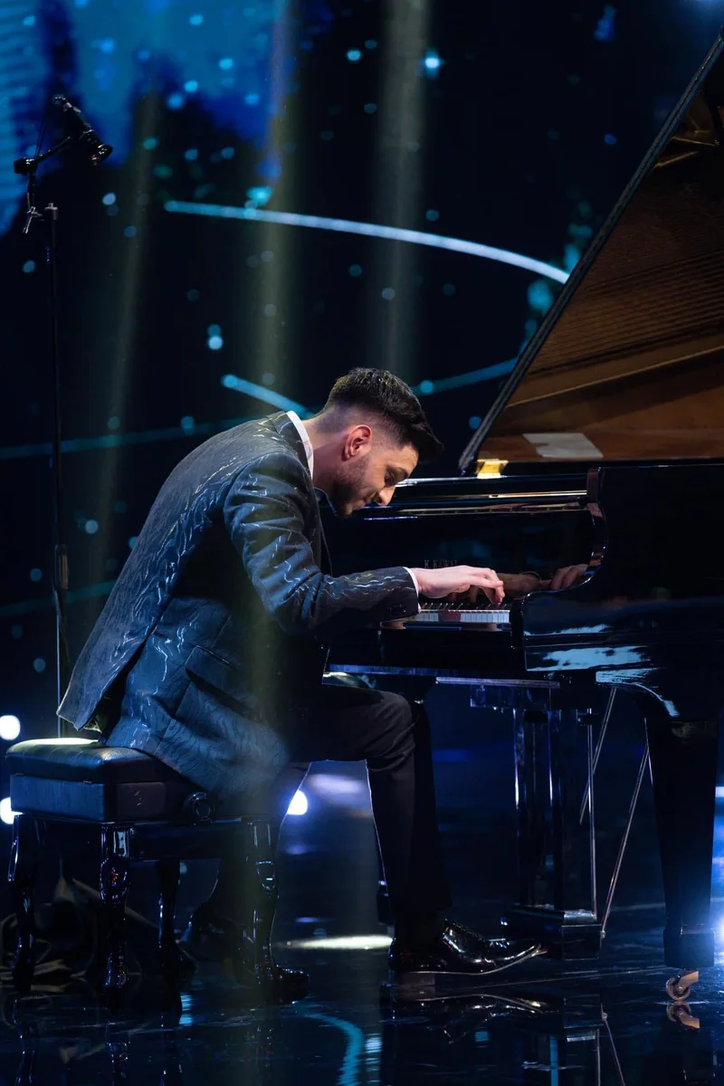 Albert Gugulan at the piano in a vertical stage photograph.